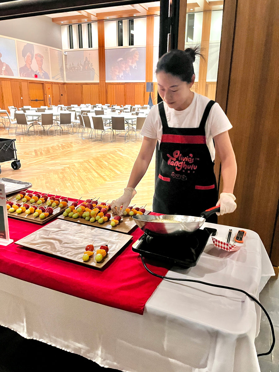 Olivia hand-glazing fresh-fruit tanghulu at a live catering station during a Bay Area event