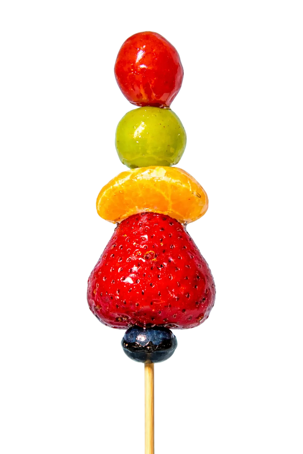 Sugar glazed fruit skewer with red strawberry, yellow orange, green grape, and red tomato on a light blue background