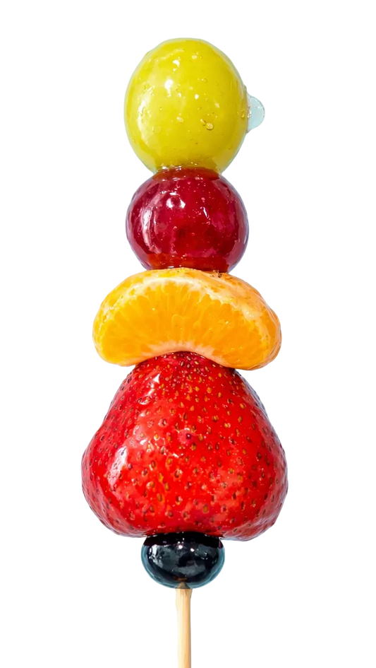 Sugar glazed Fruit skewer with a strawberry, orange slice, red grape, and   green grape on a light blue background